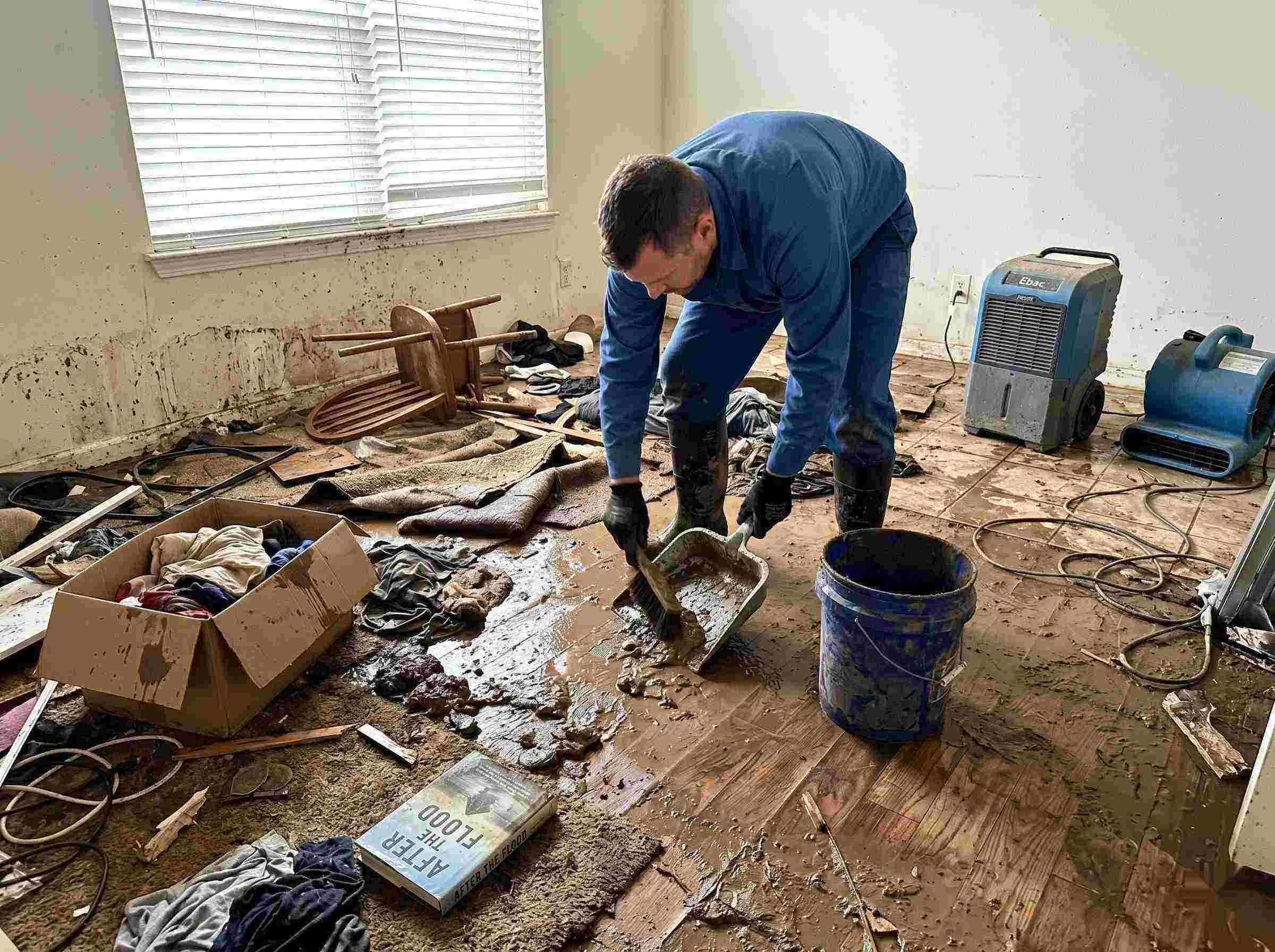 Best realistic photo of a technician performing mud and debris removal after a home flood in Kettering, showing soaked furniture, wet flooring, and scattered debris during post-flood cleanup.